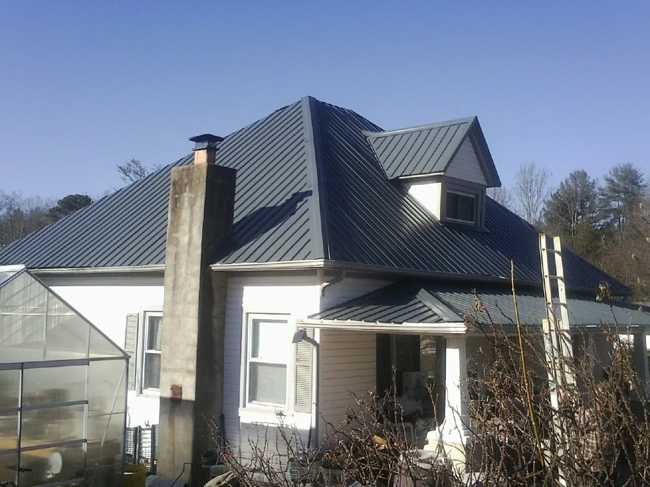Dark blue standing seam metal roof on a white farmhouse with dormer — Slate & Tile Roof Repair by Roofing Brothers in White Pine