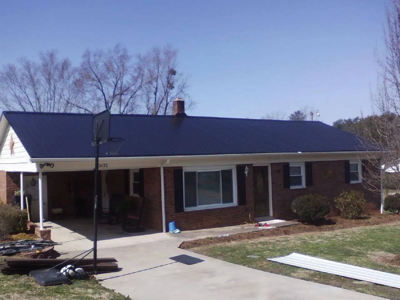 Finished dark blue metal roof on a brick ranch with a carport in White Pine