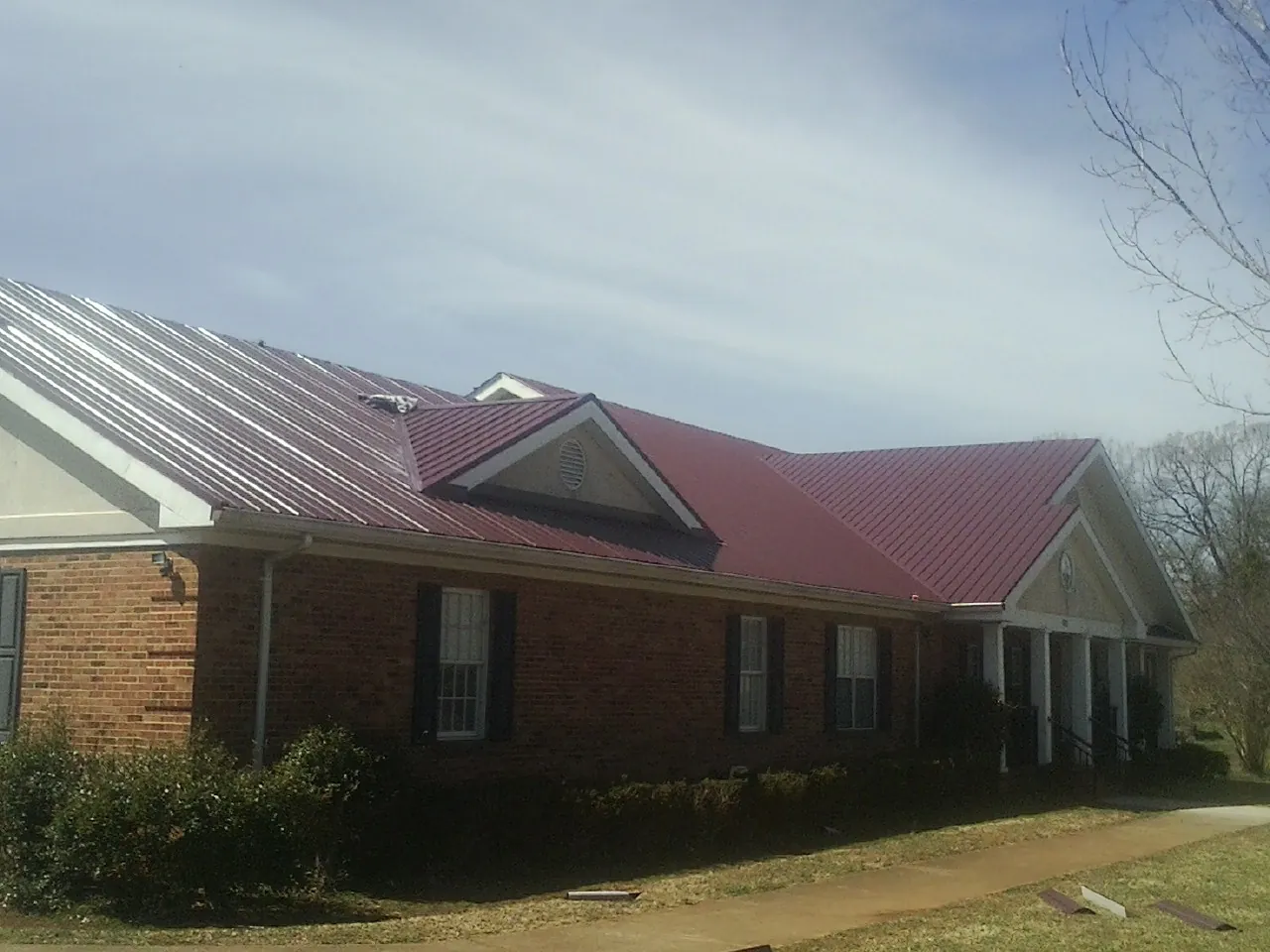 Red metal roof with gabled entries on a long brick building, from a Hail Damage Roof Repair job in White Pine