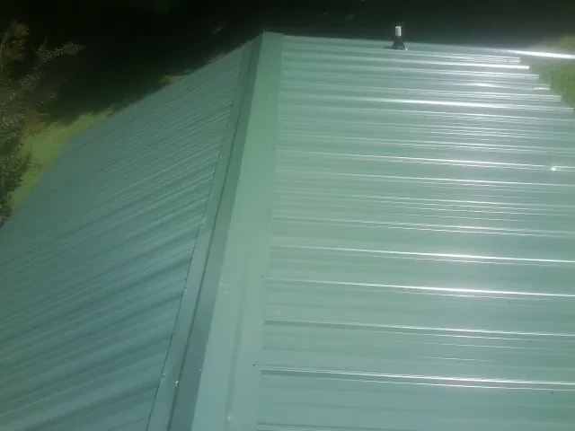 New green metal panels meeting at the ridge of a roof — Flat Roof Repair work by our crew in White Pine